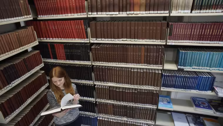 A woman reading a book in front of a bookshelf