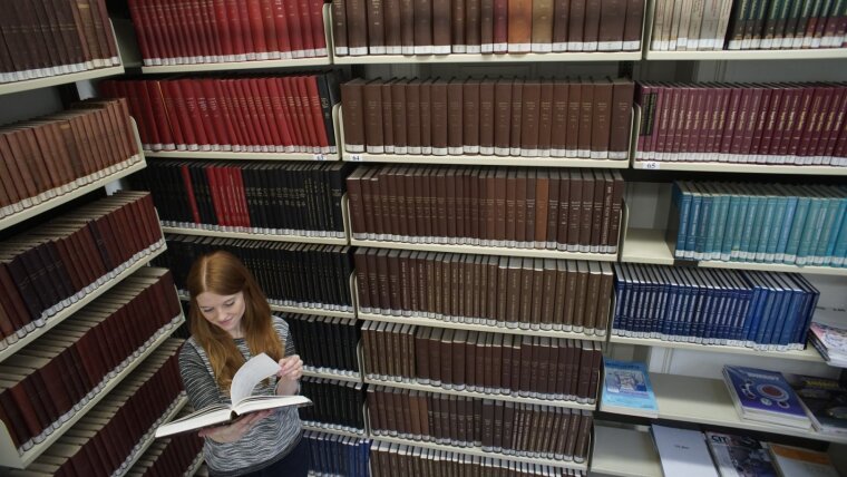 A woman reading a book in front of a bookshelf