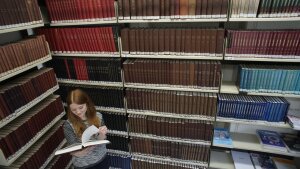 A woman reading a book in front of a bookshelf